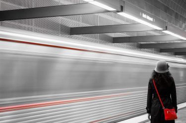 Mulher com chapéu e roupa de frio, vendo o metro passando em alta velocidade